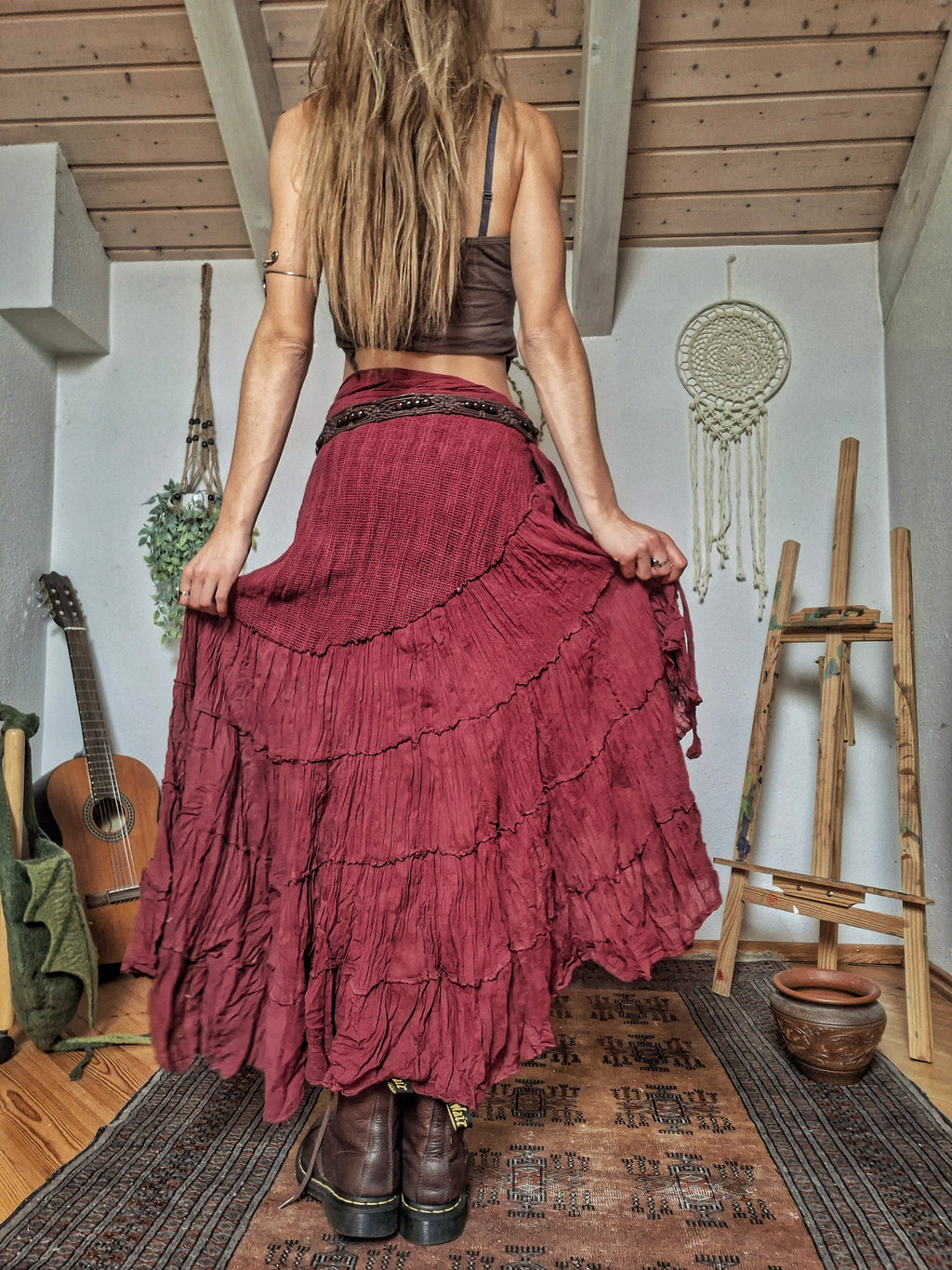 A woman viewed from behind wearing a long, tiered, deep burgundy maxi skirt with a dark brown bralette